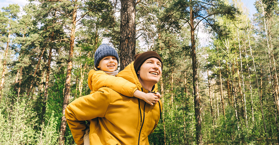 a dad walking through the forest with his son on his back