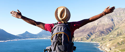A guy sitting outside looking out over a lake with his arms raised high