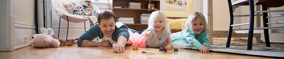 A dad laying on the floor with his 2 daughters playing with hot wheel cars