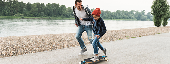 Man teaching son to skateboard next to river