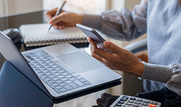 Person looking at mobile and laptop while writing