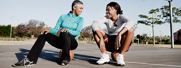 Mother and daughter sitting on basketballs