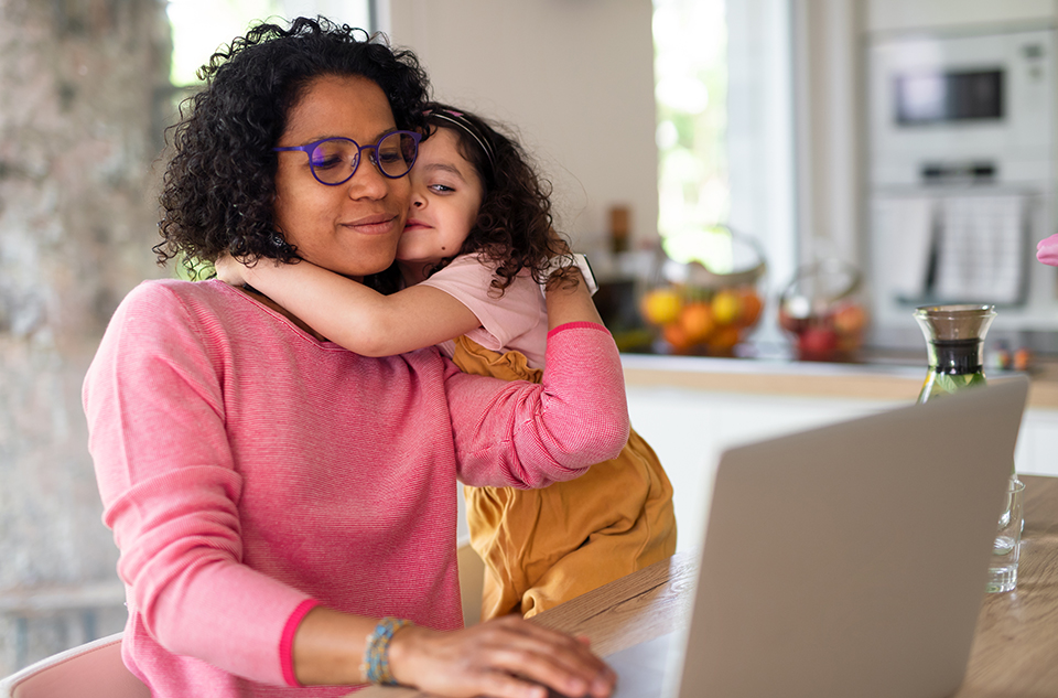 A women working on her computer with her daughter giving her a hug